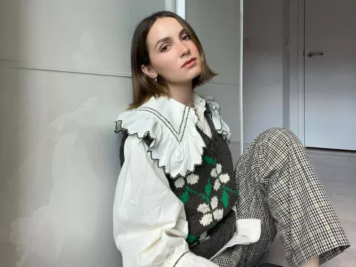 Maude Apatow wears a peter pan collar blouse, floral sweater vest, and gingham pants