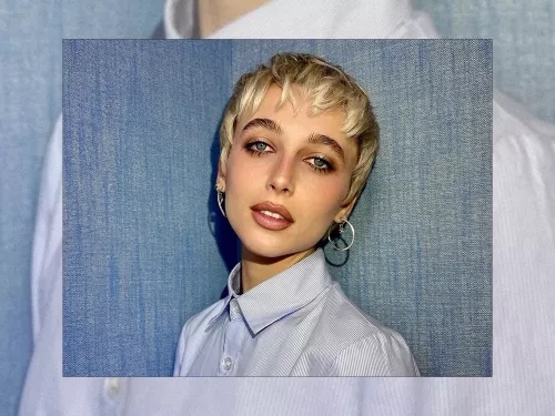 Emma Chamberlain posing in front of a blue background wearing a light shirt